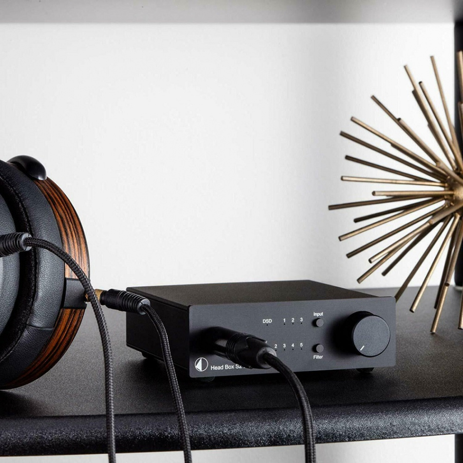 Hörlursförstärkare med DAC, ansluten till hörlurar på en hylla.