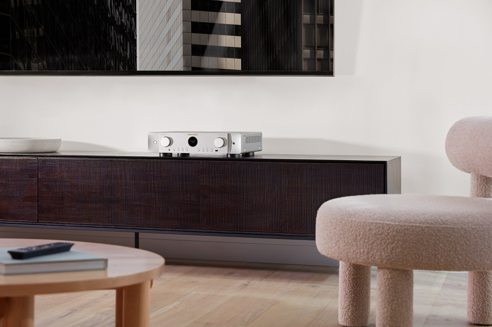 En silverfärgad hemmabioförstärkare på ett mörkt skåp i en modern inredning.