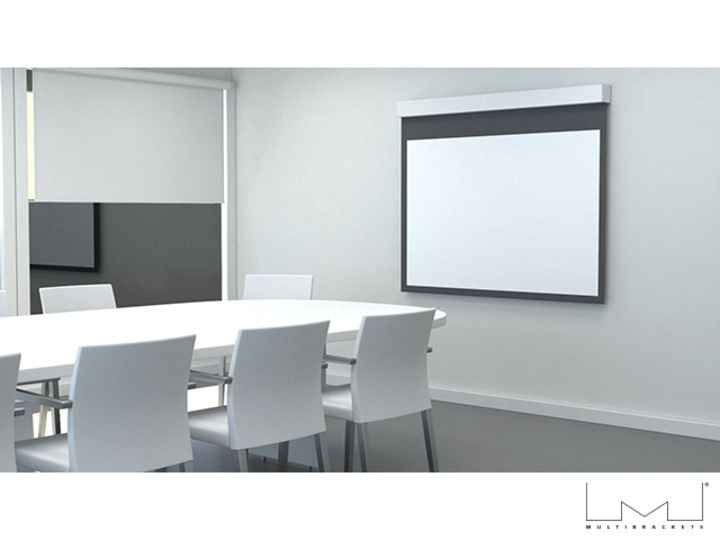 Ett konferensrum med motoriserad projektorduk på väggen och ett stort bord med stolar.