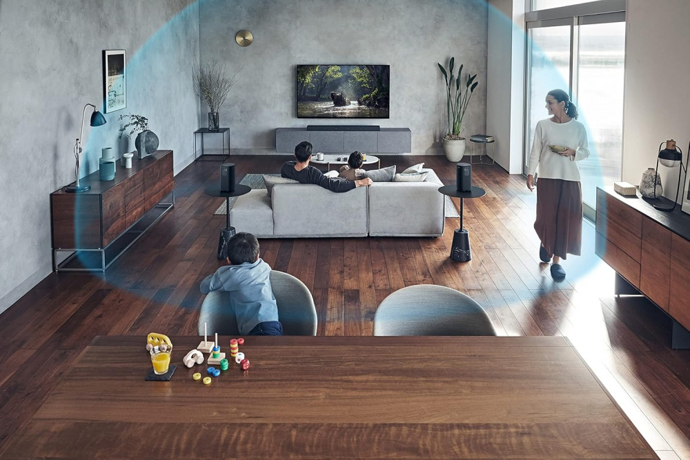 Ett modernt rum med familj som tittar på TV, omgiven av högtalare.