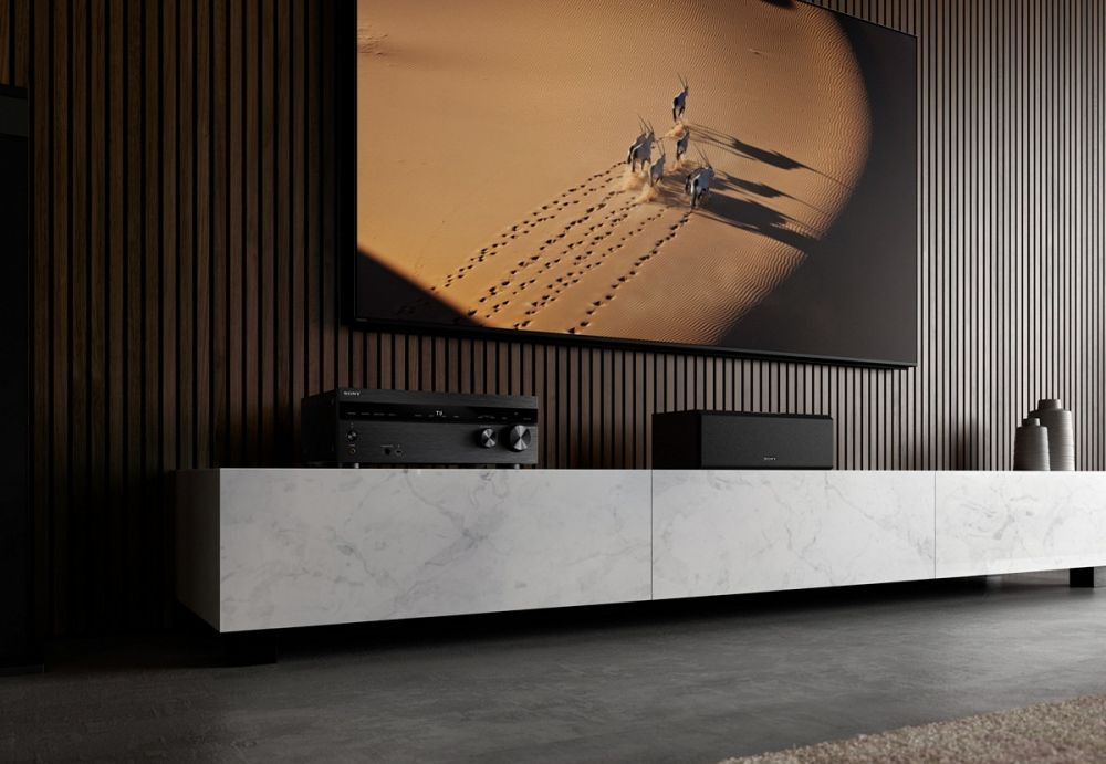 En TV på väggen, en hemmabioförstärkare och ljudsystem på ett vitt skåp.