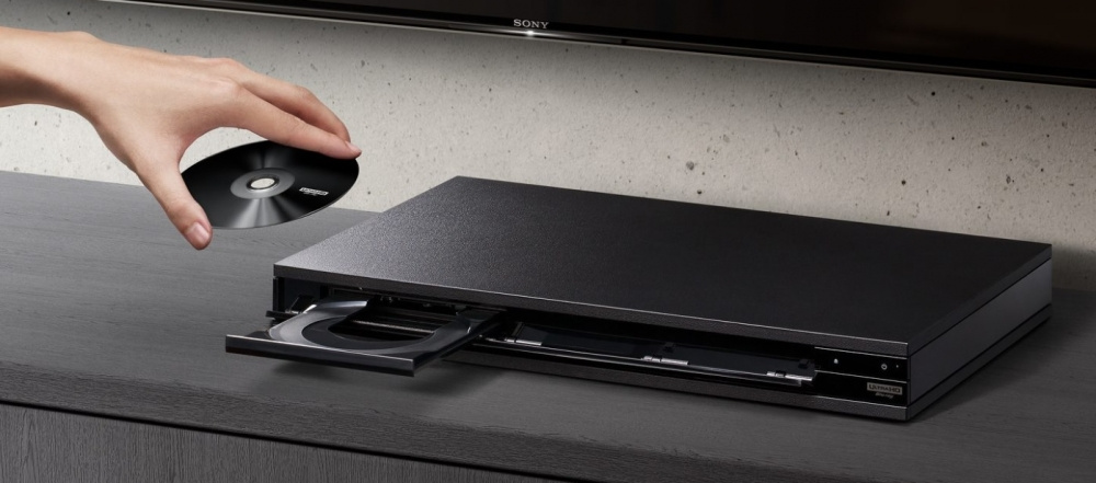 En hand håller ett skivfodral ovanför en Blu-Ray-spelare.