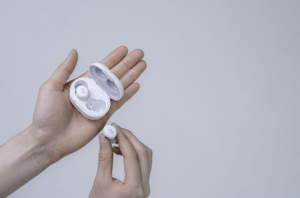 Trådlösa in-ear hörlurar i vitt i en hand, tillsammans med laddningsfodral.