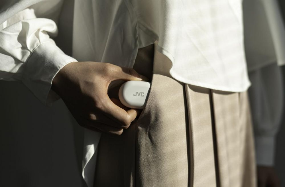 En hand håller i ett litet, vitt fodral med JVC-logotyp, som verkar innehålla hörlurar.