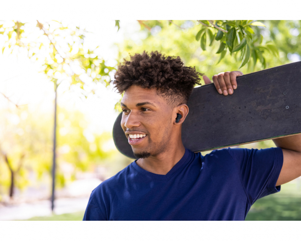 Ung man med skateboard och trådlösa hörlurar i en park.