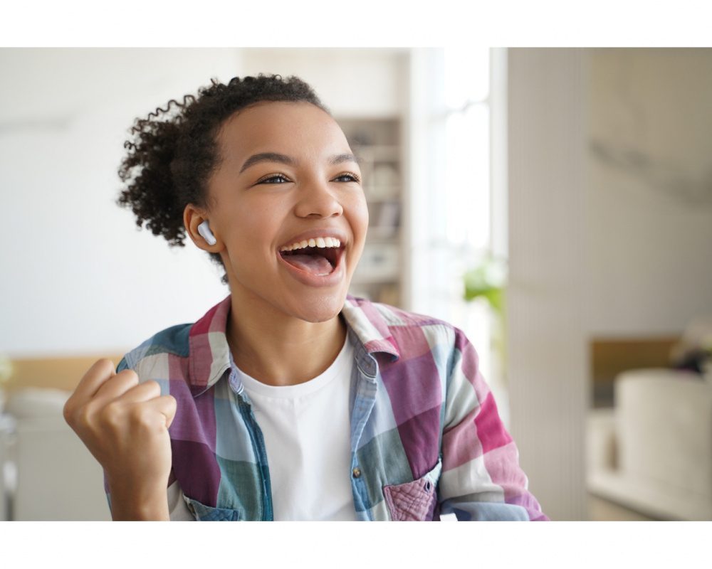 En glad person som använder trådlösa in-ear hörlurar inomhus.