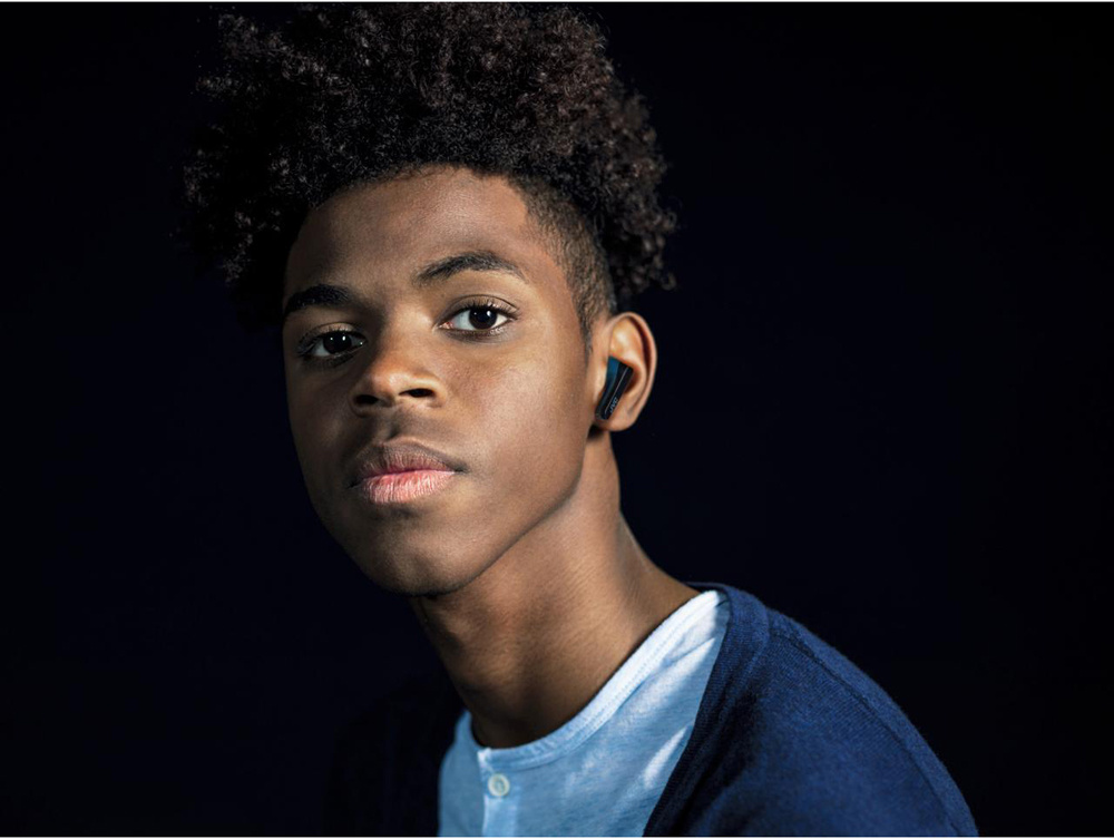 En ung kille med lockigt hår och trådlösa hörlurar i öronen.