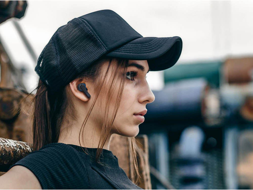 En kvinna med svart keps bär blå trådlösa in-ear hörlurar.