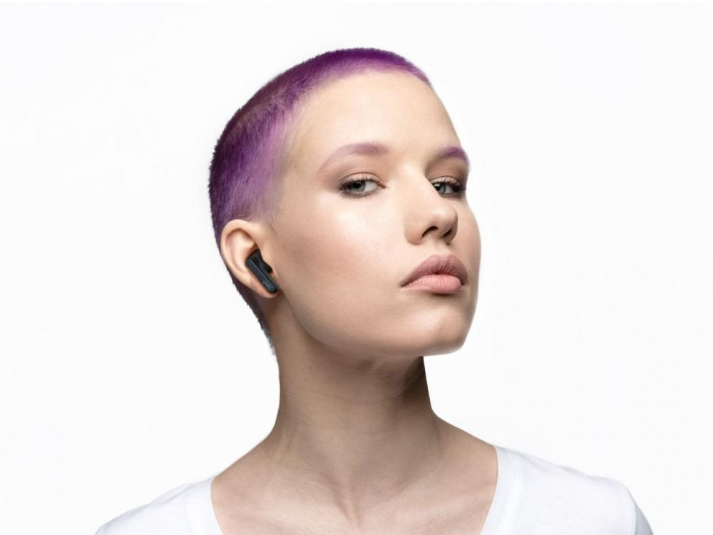 En person med kort ljust hår bär svarta trådlösa hörlurar.