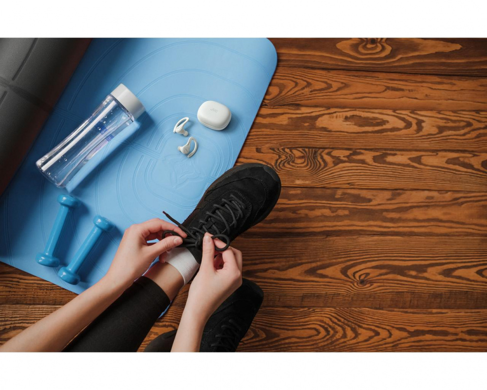 En person knyter skorna med sportutrustning och hörlurar i bild.