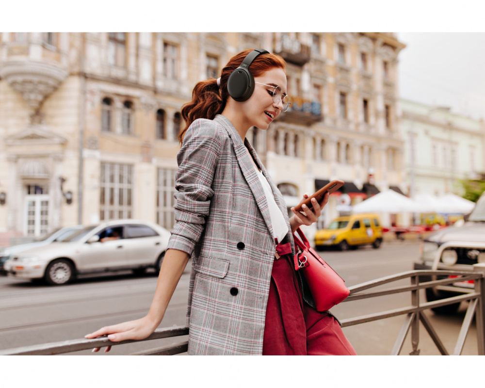Kvinna med trådlösa hörlurar och smartphone i stadsmiljö.