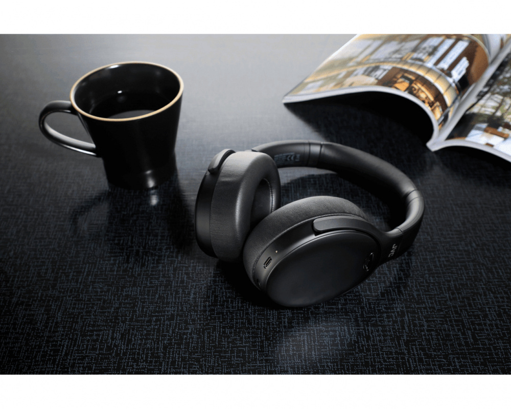 Trådlösa hörlurar ligger på ett bord bredvid en svart kopp och en tidning.