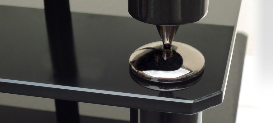 En del av en svart TV-bänk med metallfötter och en reflekterande yta.