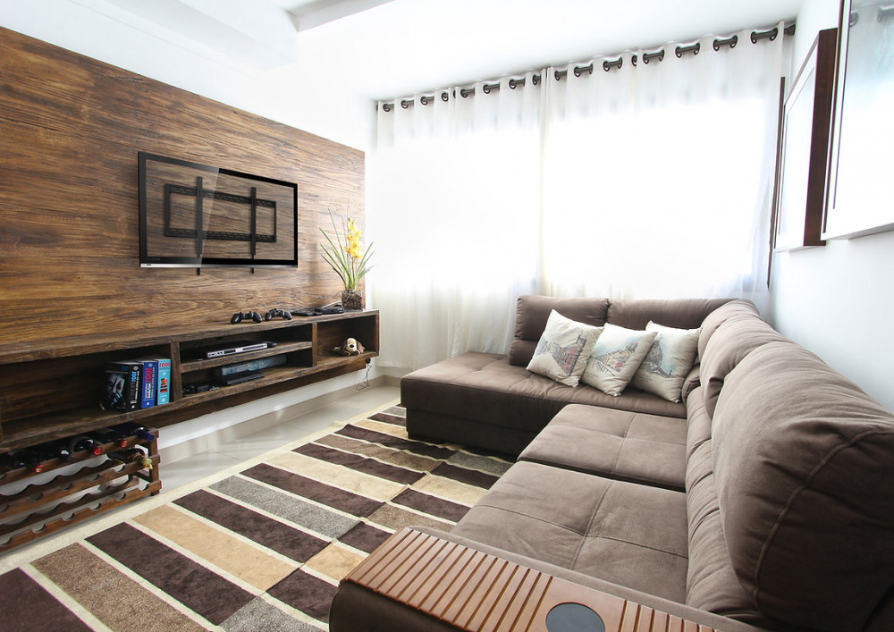 Ett rum med en TV på väggen, en soffgrupp och en trähylla.