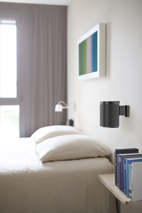 Justerbart väggfäste för högtalare, placerat vid säng i modern inredning.