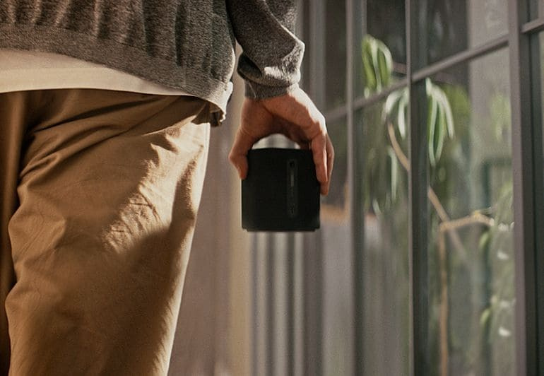 En person håller en svart trådlös högtalare i handen.