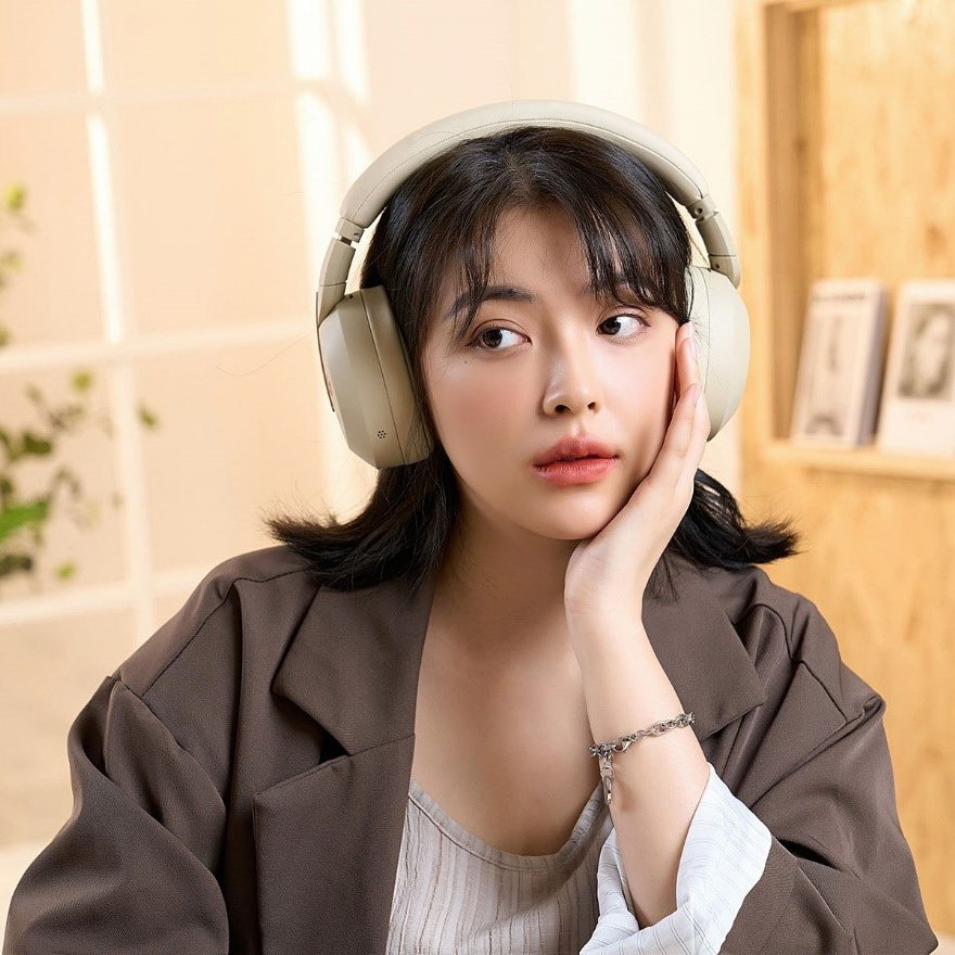 En kvinna med beige hörlurar i en modern, ljus inredning.