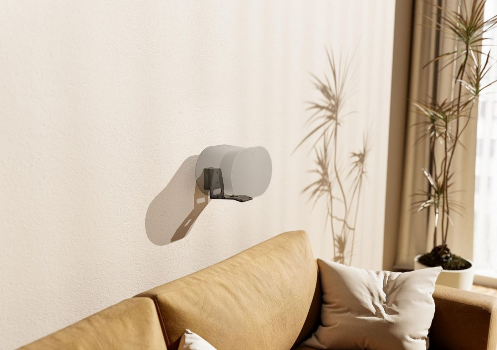 Svart väggfäste för Sonos Era 300 monterat på en ljus vägg ovanför en soffa.