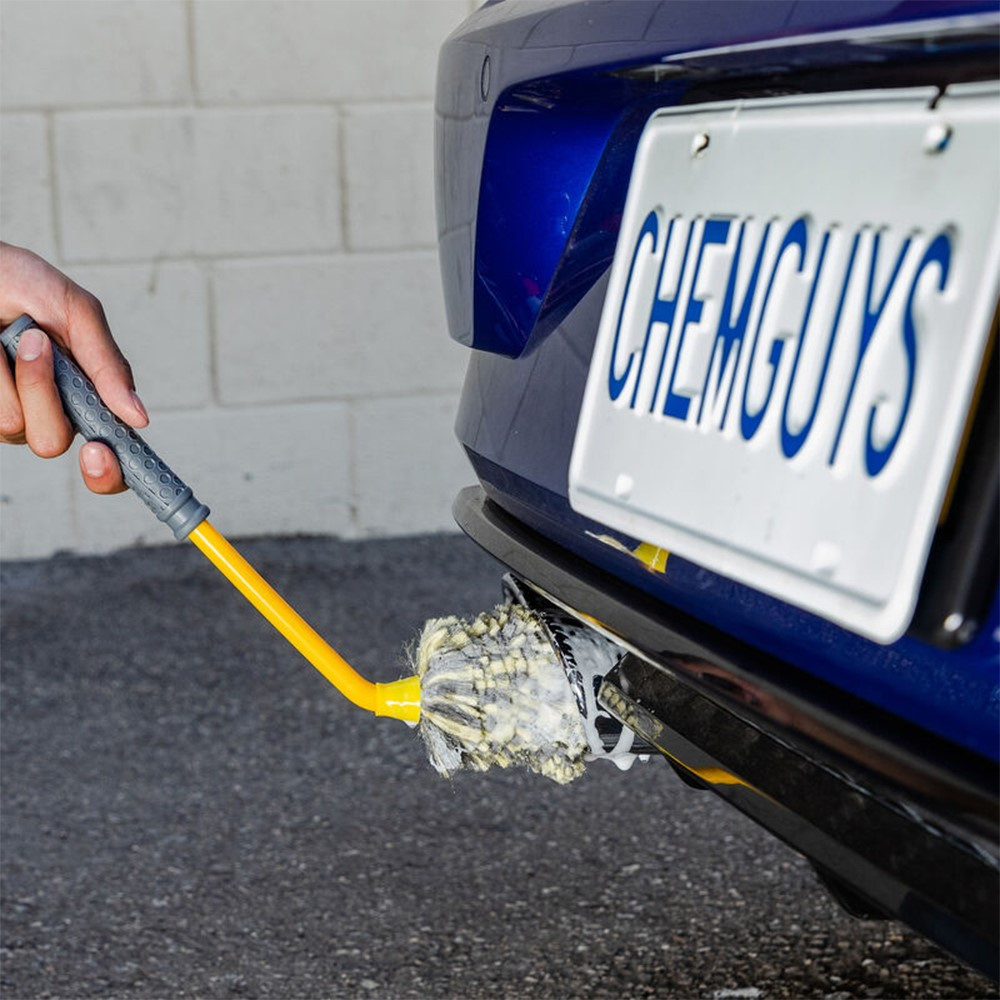 En hand som använder en gul och grå borste för att rengöra en bil.