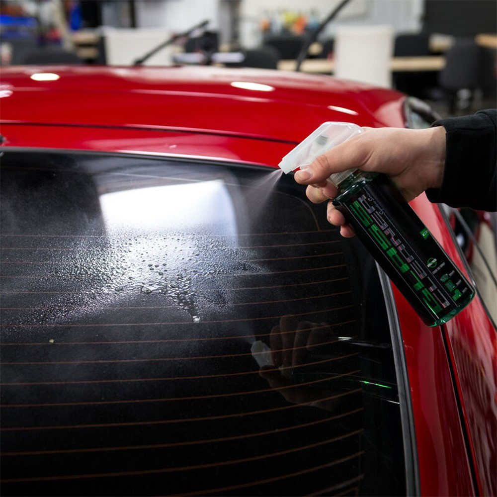 En hand sprayar glasrengöring på en bilruta.