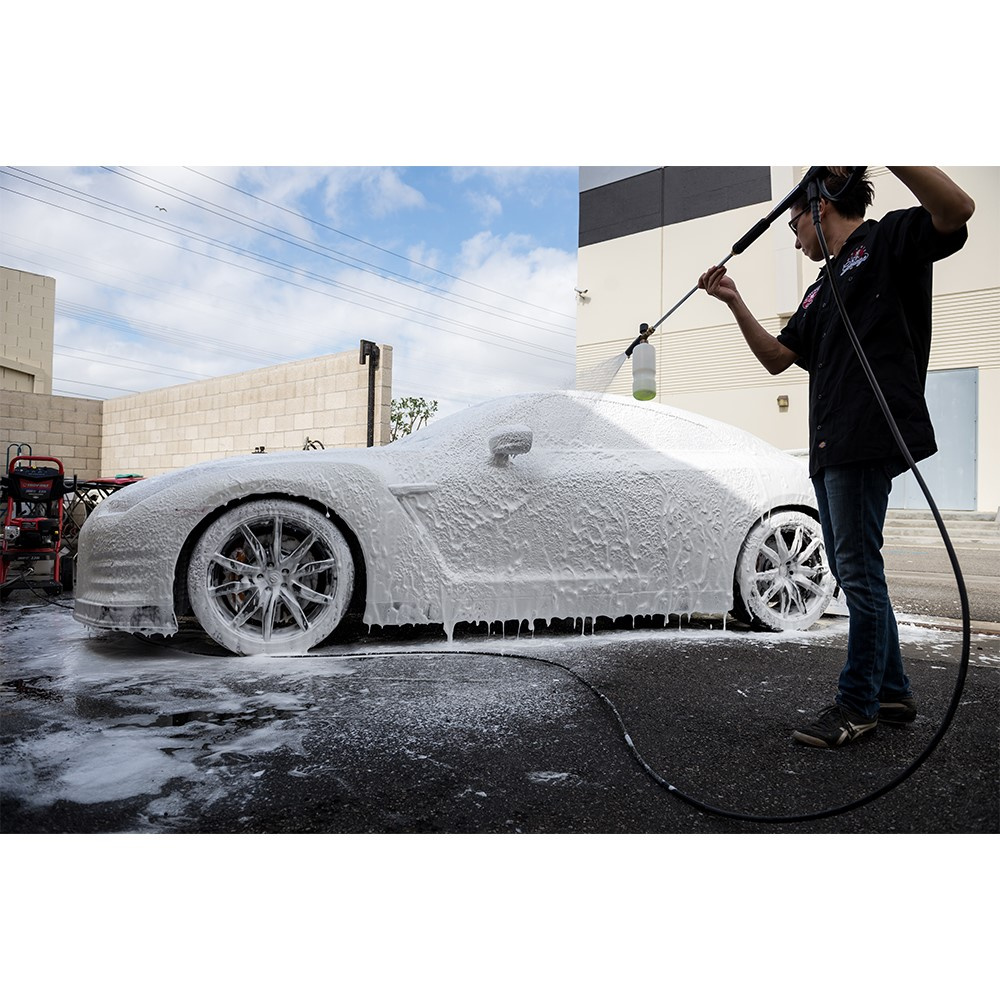 En bil täckt av skum medan en person sprutar schampo på den.