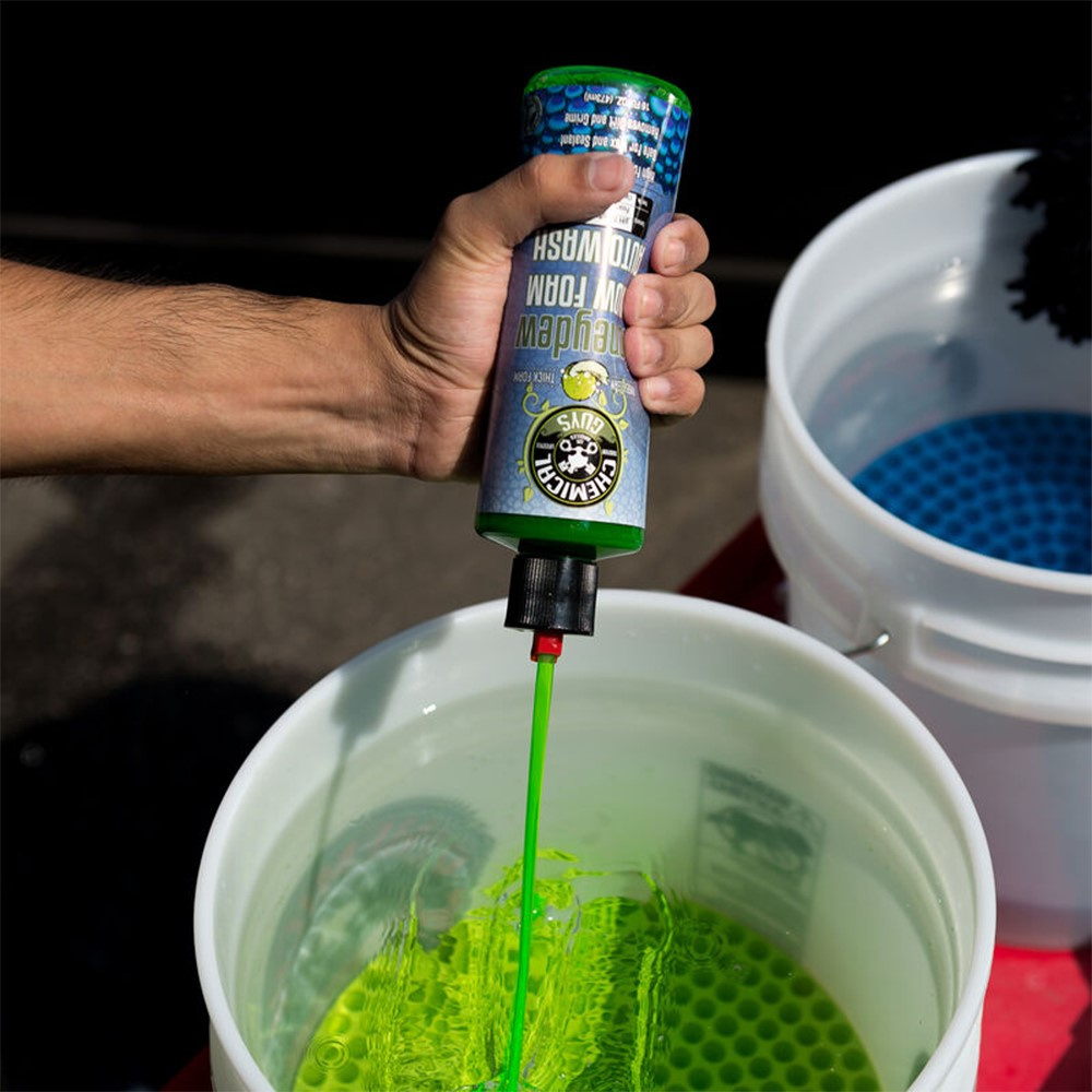 En hand håller en flaska skummande bilschampo över en hink med vatten.