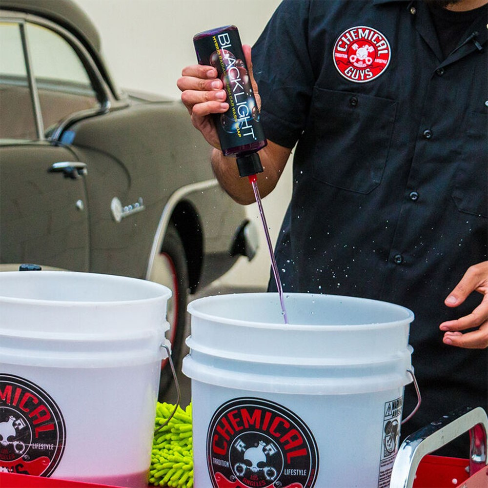 En person häller lila bilschampo i en hink.