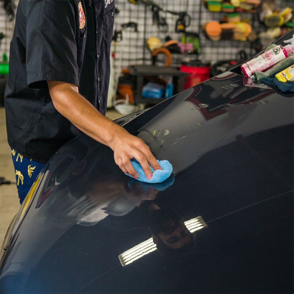 Hand håller en blå mikrofiberapplikator på en bils lack.