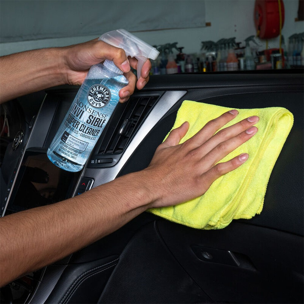 En hand sprayar rengöringsmedel på en bilinteriör med en gul trasa.