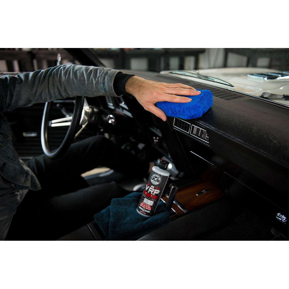 En person applicerar en plastvård på bilens interiör med en blå trasa.