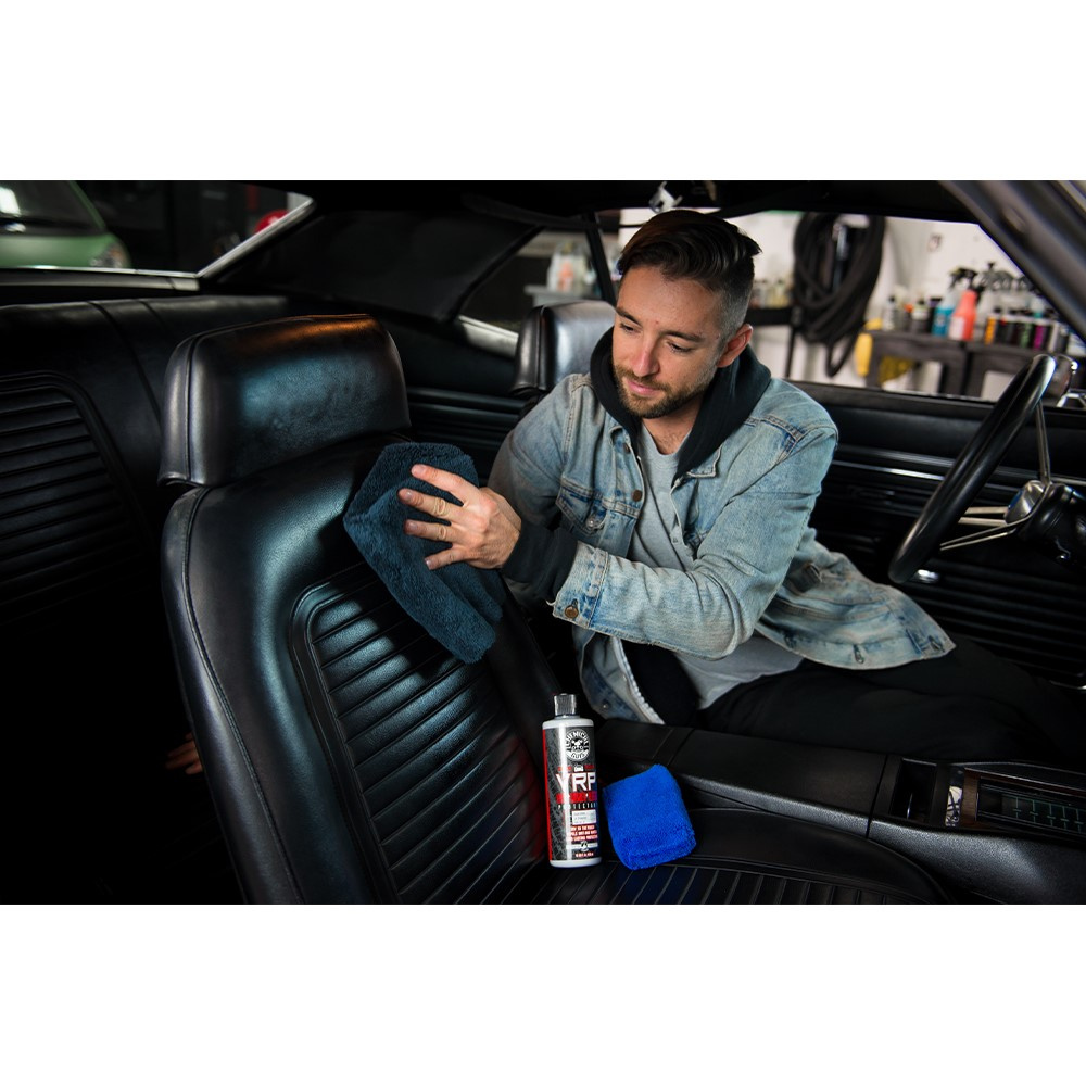 En man applicerar bilprodukten på en svart lädersäte inuti en bil.