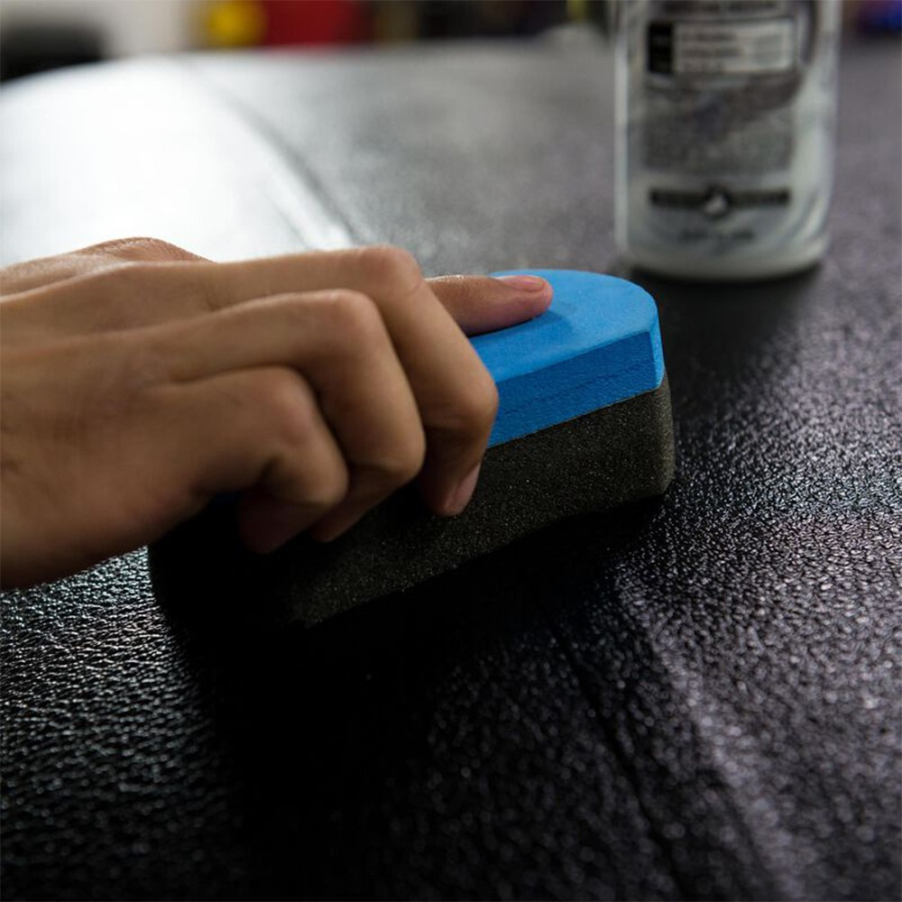 En hand applicerar en glansdressing med en svamp på en yta.