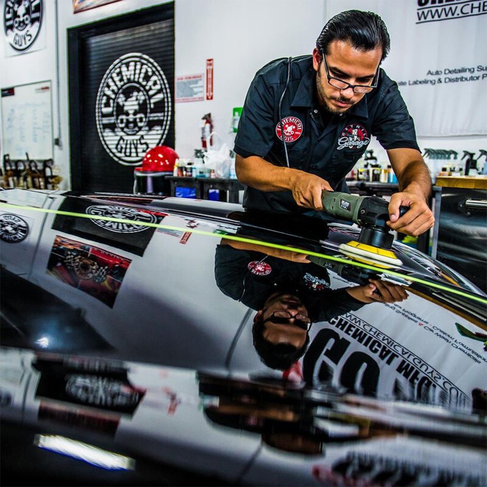 En person polerar en svart bil med en maskin i en bilvårdsverkstad.