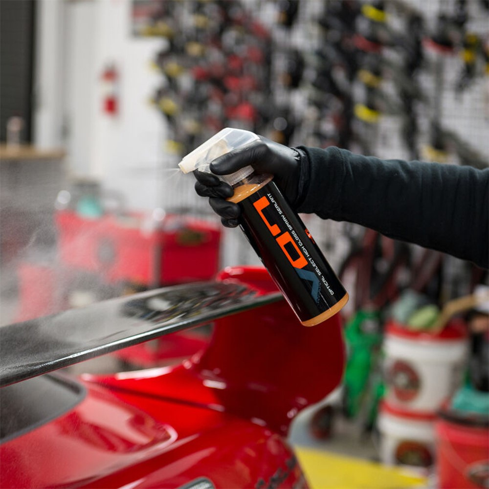 En person sprayar ett glänsande bilvårdsmedel på en röd bil.