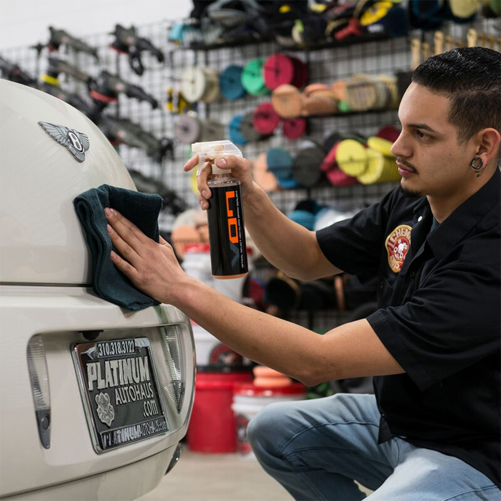 En man applicerar bilvårdsspray på en bils baklucka.