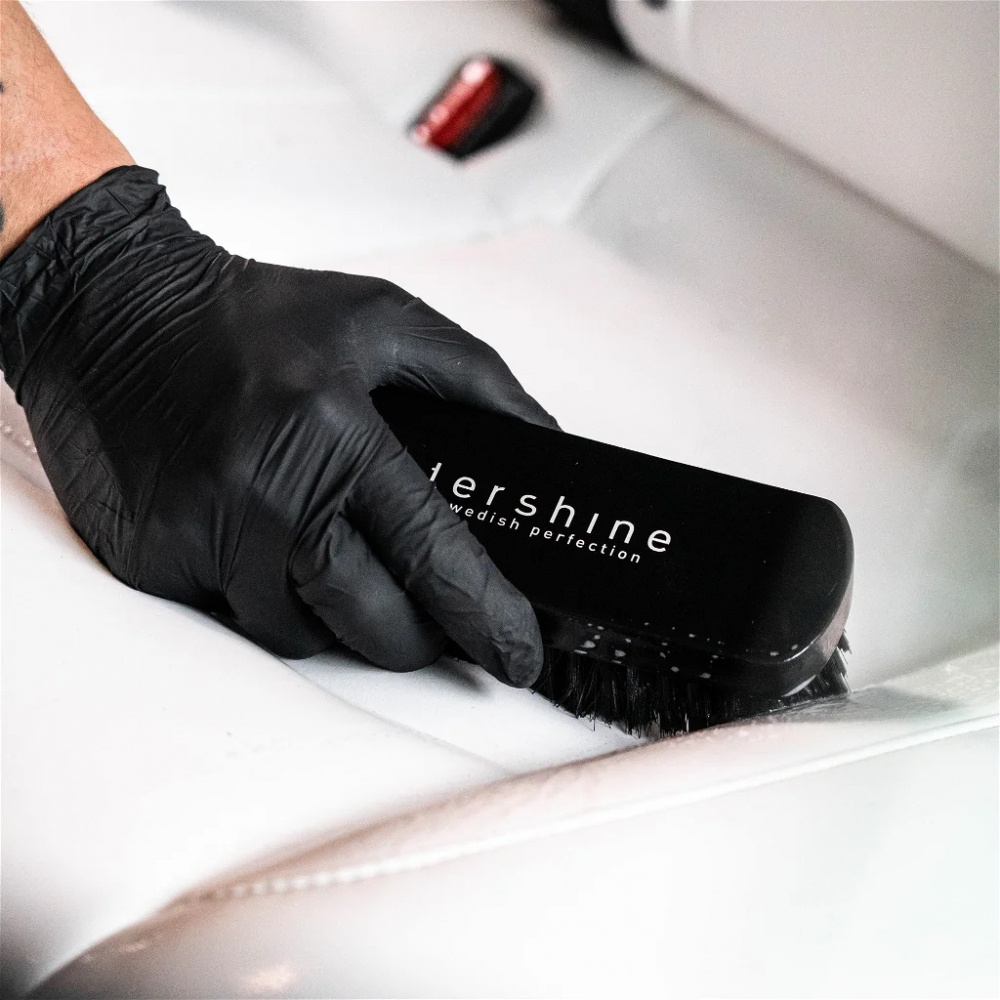 En hand i svart handske som använder en rengöringsborste på en vit yta.