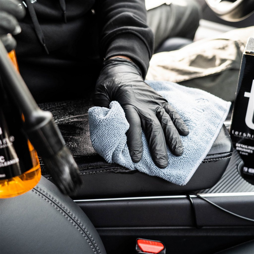 En hand med svart handske håller en blå trasa på en bilinteriör.