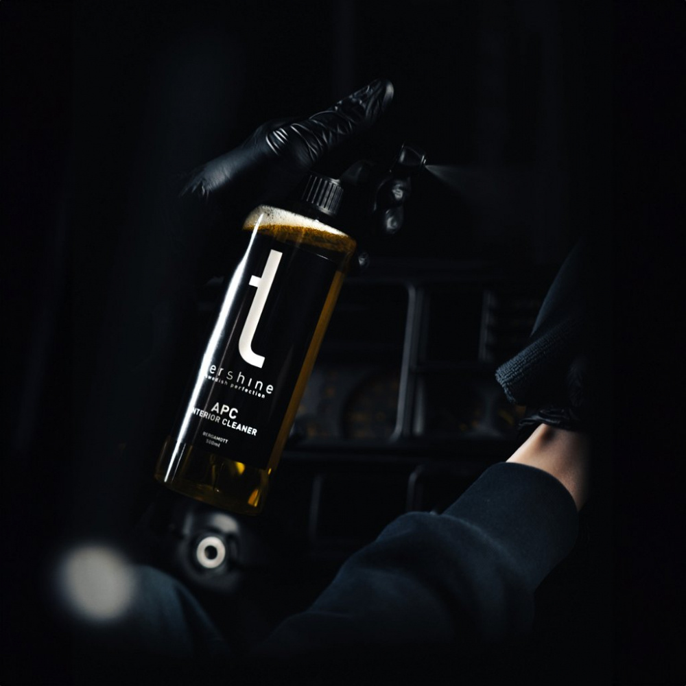 En hand håller en sprayflaska med allrengöring i en mörk bilinteriör.