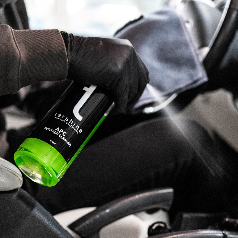 En person sprutar en grön flaska med rengöringsmedel i en bil.