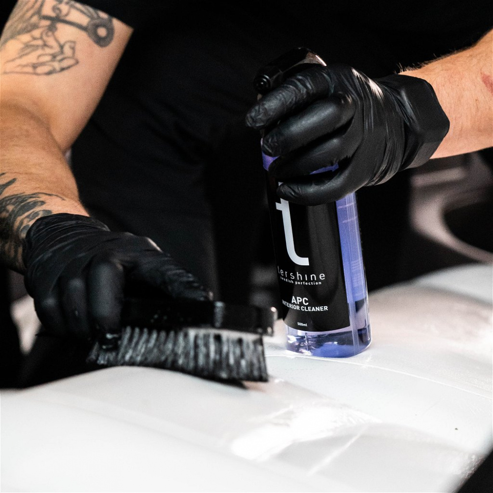 En person använder Tershine APC rengöringsspray med en borste på en vit yta.