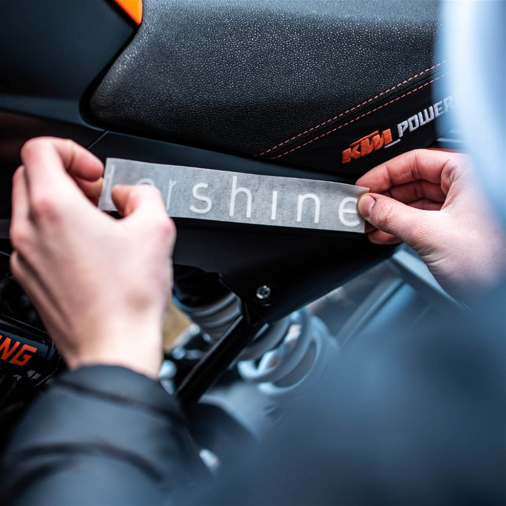 En person fäster en svart Tershine-dekal på en motorcykel.