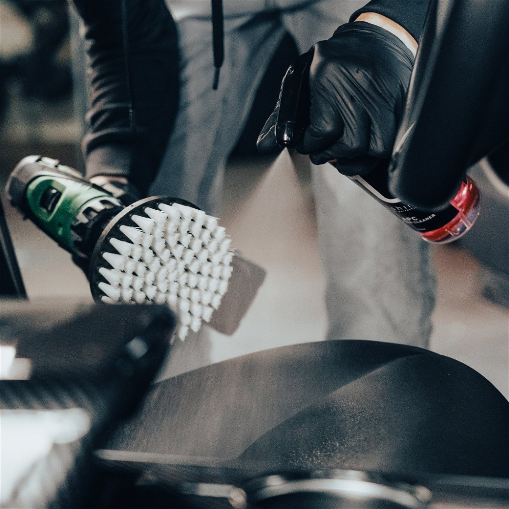 En person använder en skruvdragare med en rengöringsborste för att putsa en yta.
