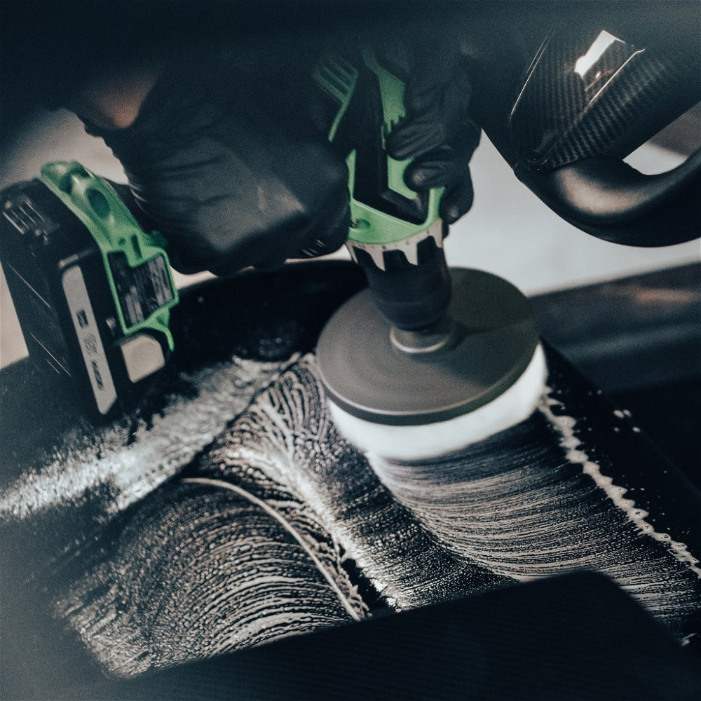 En person använder en skruvdragare med en borste för att rengöra en yta.