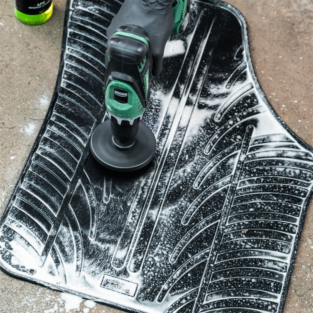 En skruvdragare rengör en gummimatta med borstar och schampo.