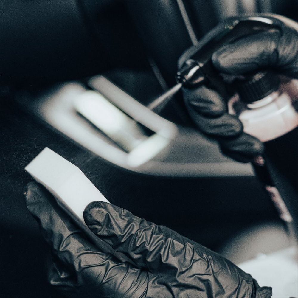 En hand i svart handske håller en rengöringssvamp och sprayflaska.