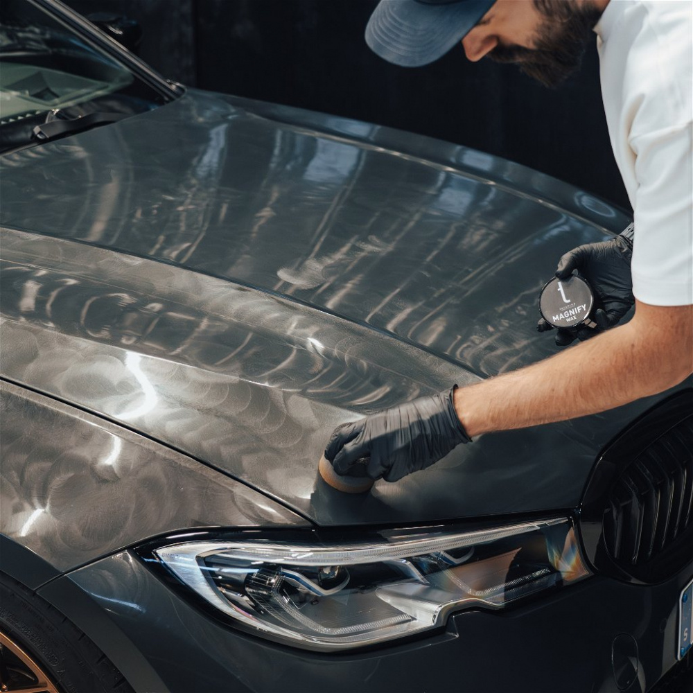 En person applicerar ceramisk wax på en bils motorhuv.