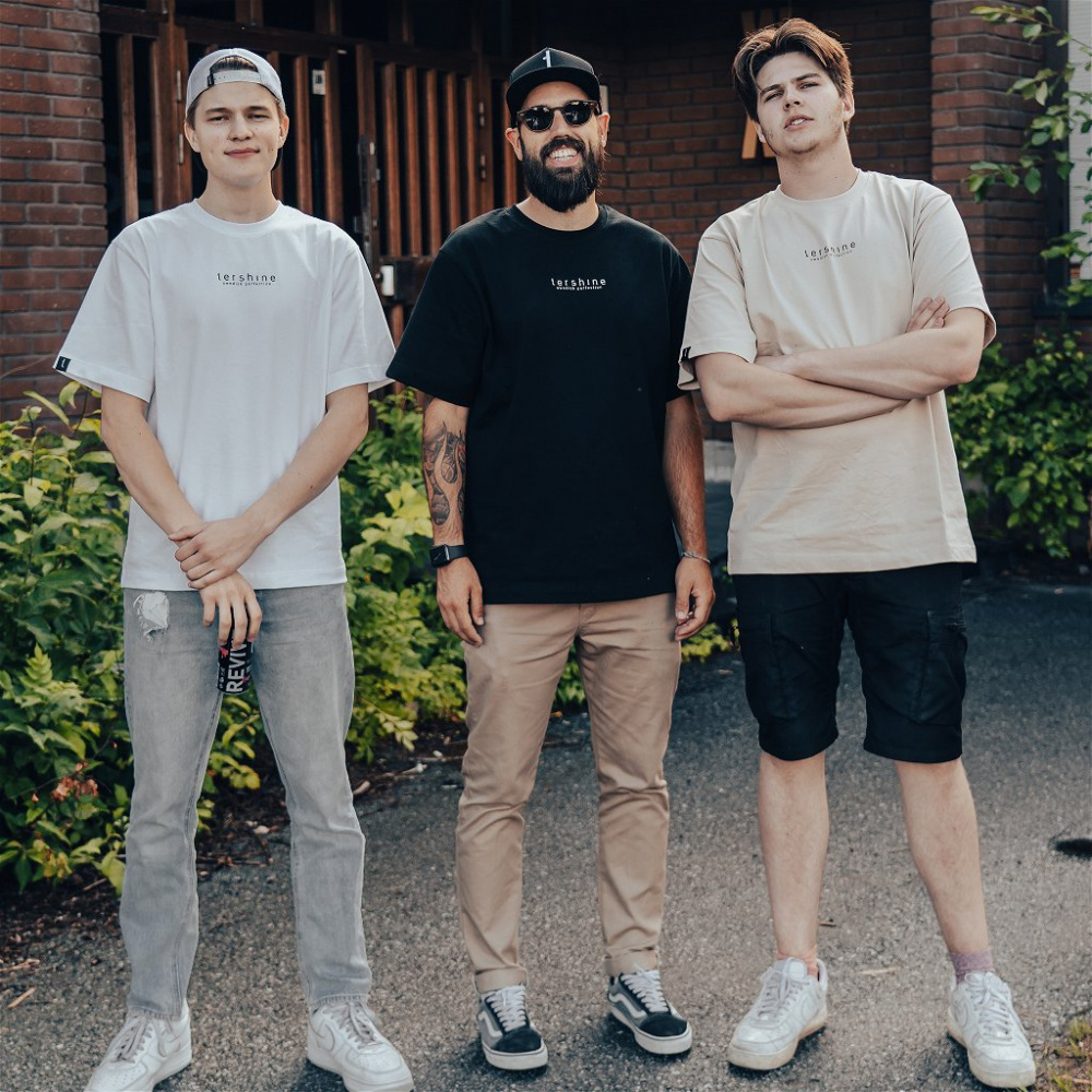 Tre män står tillsammans utomhus, klädda i T-shirts och shorts.