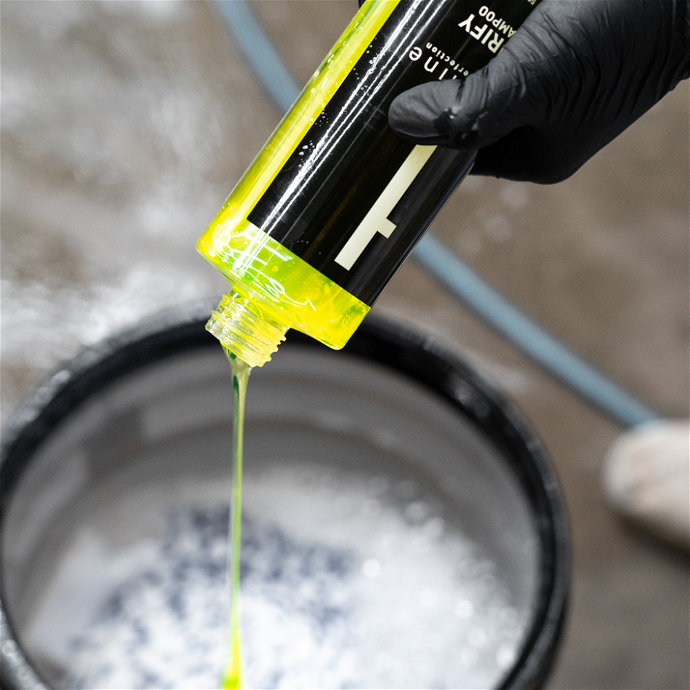 Flaskan med gult schampo hälls över ett schampobad.