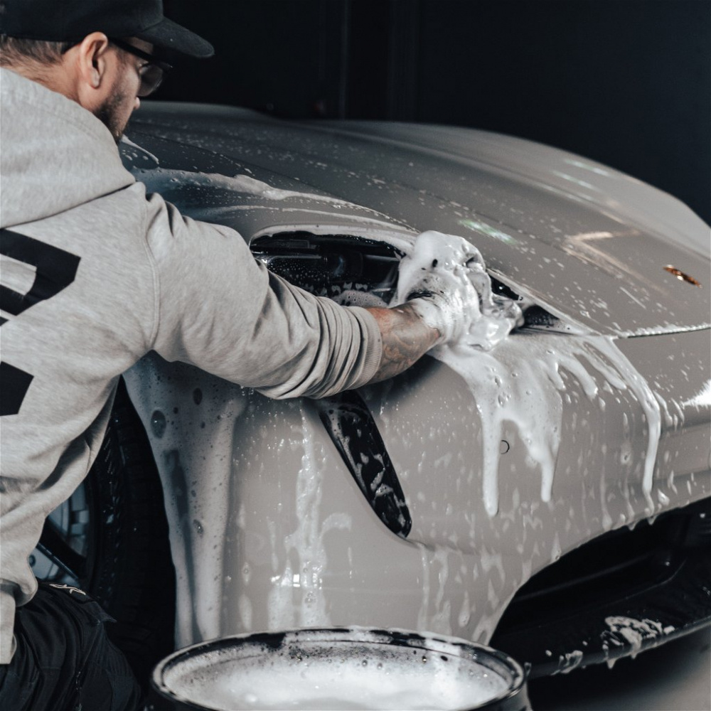 En person rengör en bil med schampo och skum.