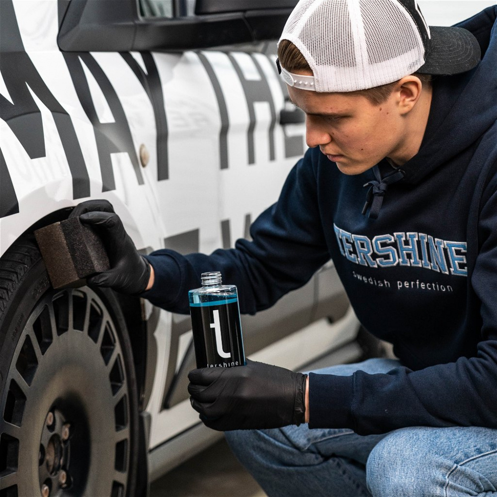 En man applicerar däckglans på en bil med en svamp.